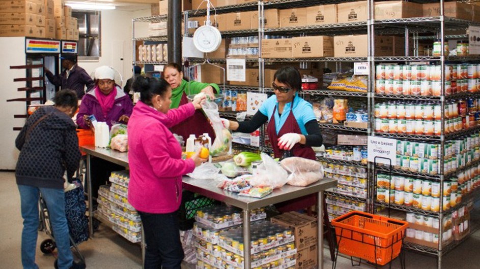 A group of women volunteering at a food pantry, giving out groceries. 