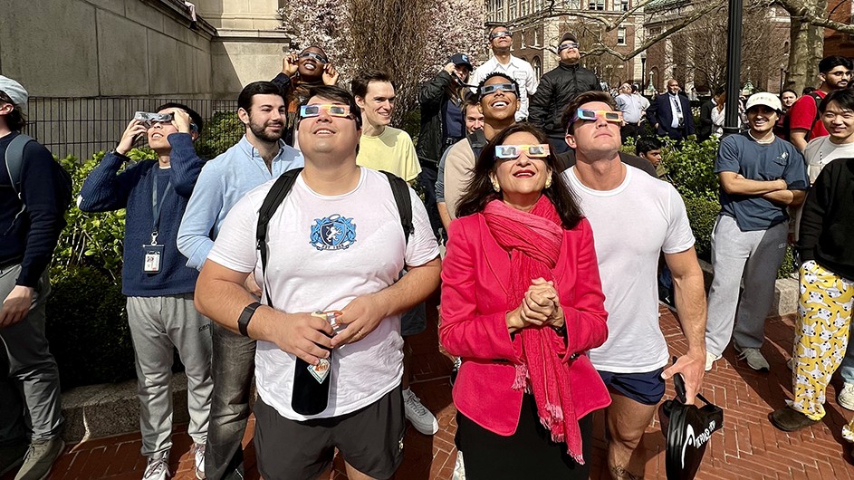 A group of people wearing blackout glasses looking up. 
