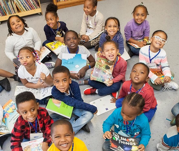 A group of kids lifting their heads up from their books to smile and pose for the camera