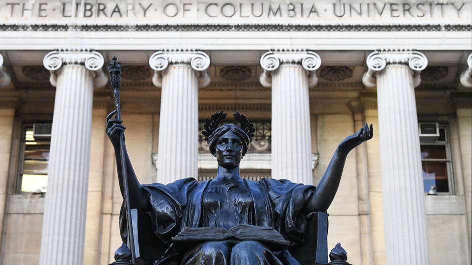 Front view of bronze statue of Alma Mater, a woman on a throne with a laurel wreath in her hair and a scepter in her hand, against the backdrop of the white columns of Low Library under the words, "The Library of Columbia University."