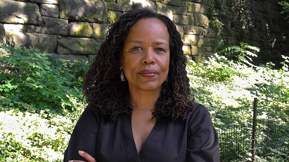 Photo credit the MacArthur Foundation Photo of a woman with long dark hair, in a black outfit standing outside against a backdrop of green grass.