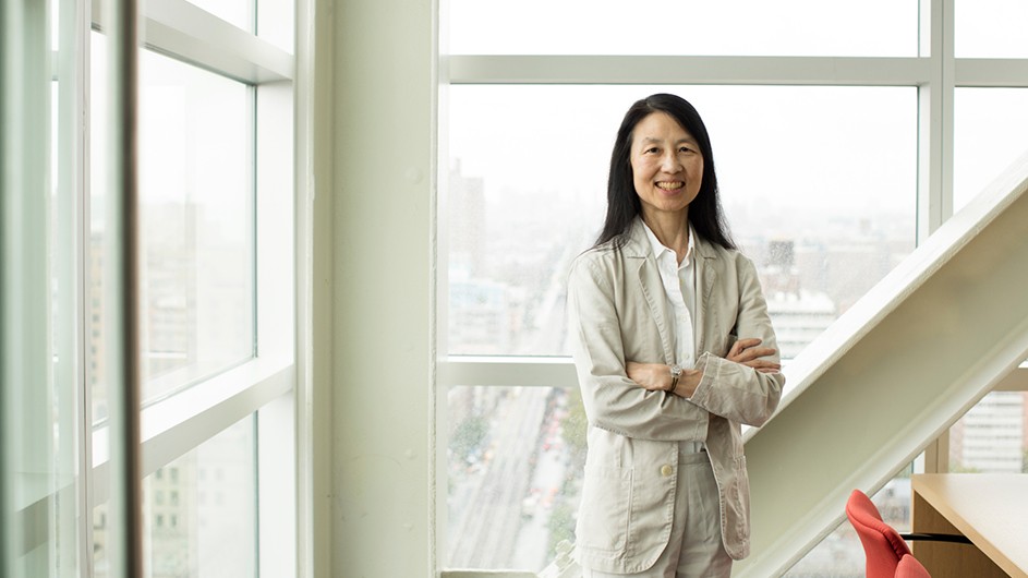 Woman in a white suit standing inside against a backdrop of big, white windows.