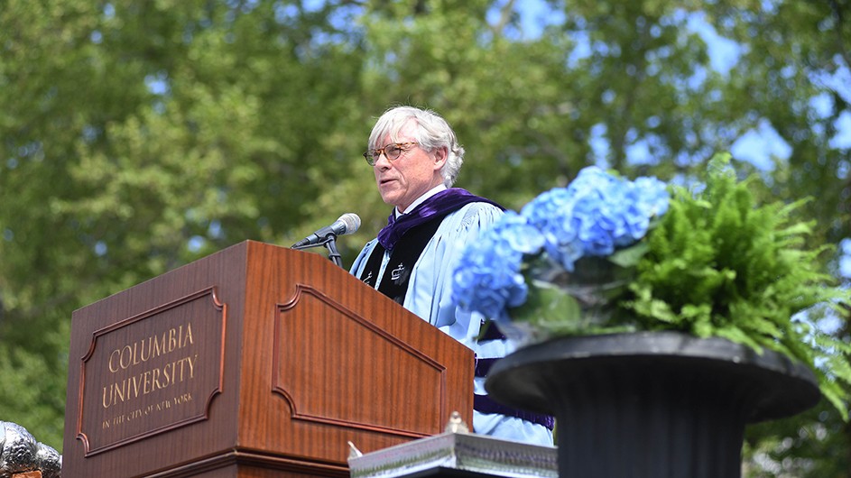Photo: Eileen Barroso. Lee C. Bollinger, a man in a light blue graduate robe, standing at a podium during Columbia's Commencement.