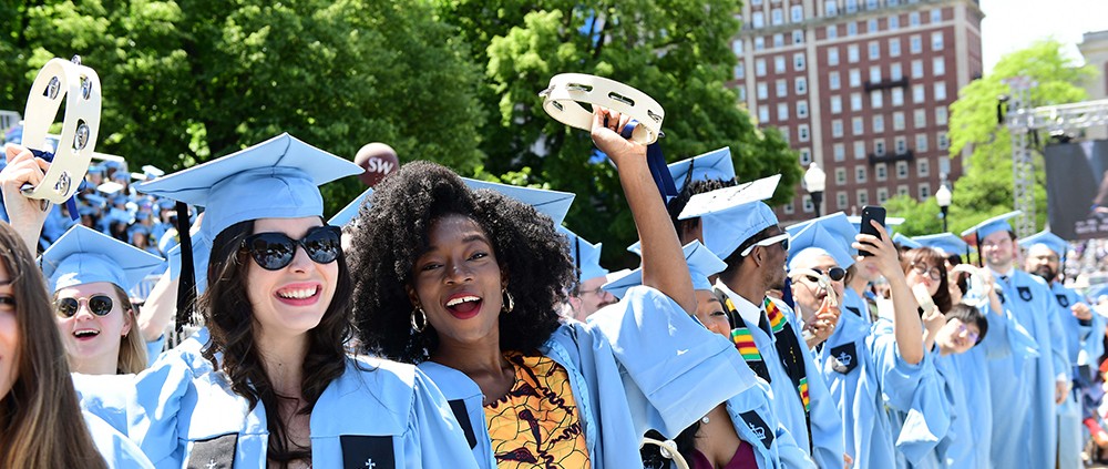 Photo of students in academic regalia, celebrating with tambourines. at Commencement