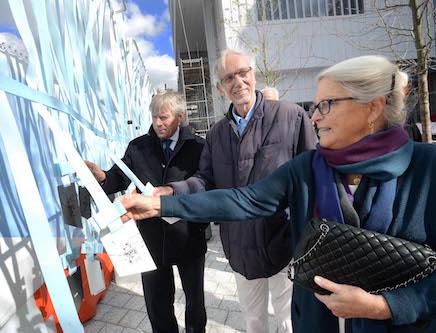 Jean Magnano Bollinger (right) holds a badge from a wall of badges with blue ribbons in front of architect Renzo Piano (center) and President Lee Bollinger (left)