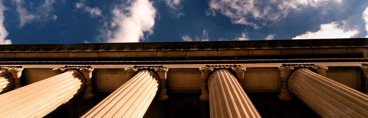 Blue sky with clouds framed by a view looking straight up at the classical, marble columns of Low Library.
