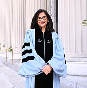 Minouche Shafik, a woman with long dark hair and glasses, smiling.