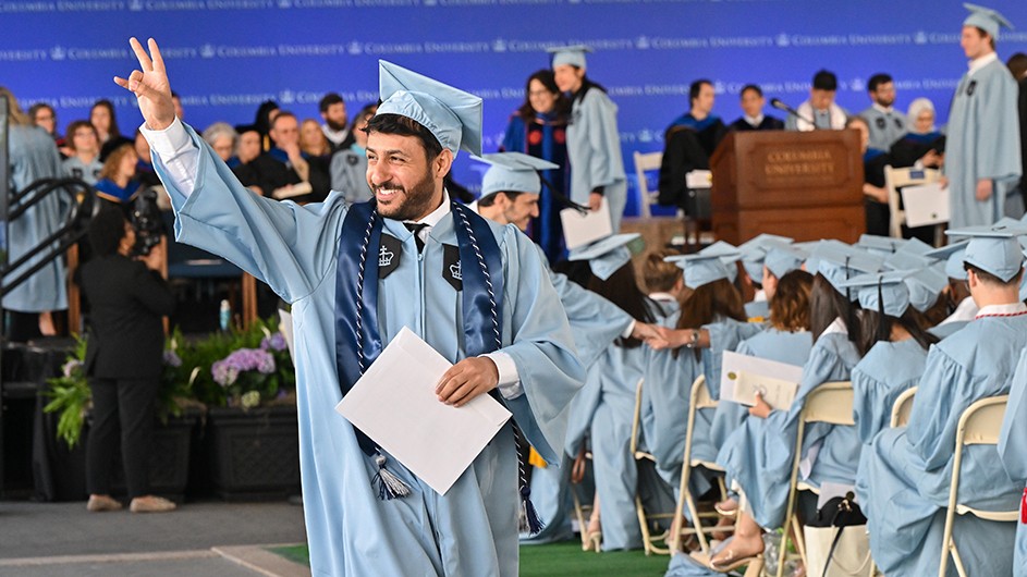 A student flashes the peace sign (two fingers) while processing at a graduation ceremony.