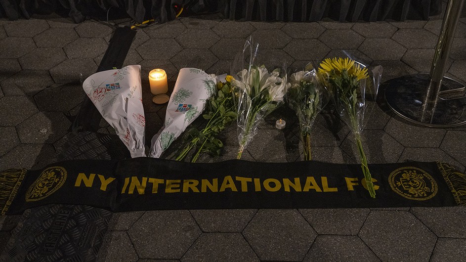 Flowers and a candle above a black and yellow banner that says "NY International FC"