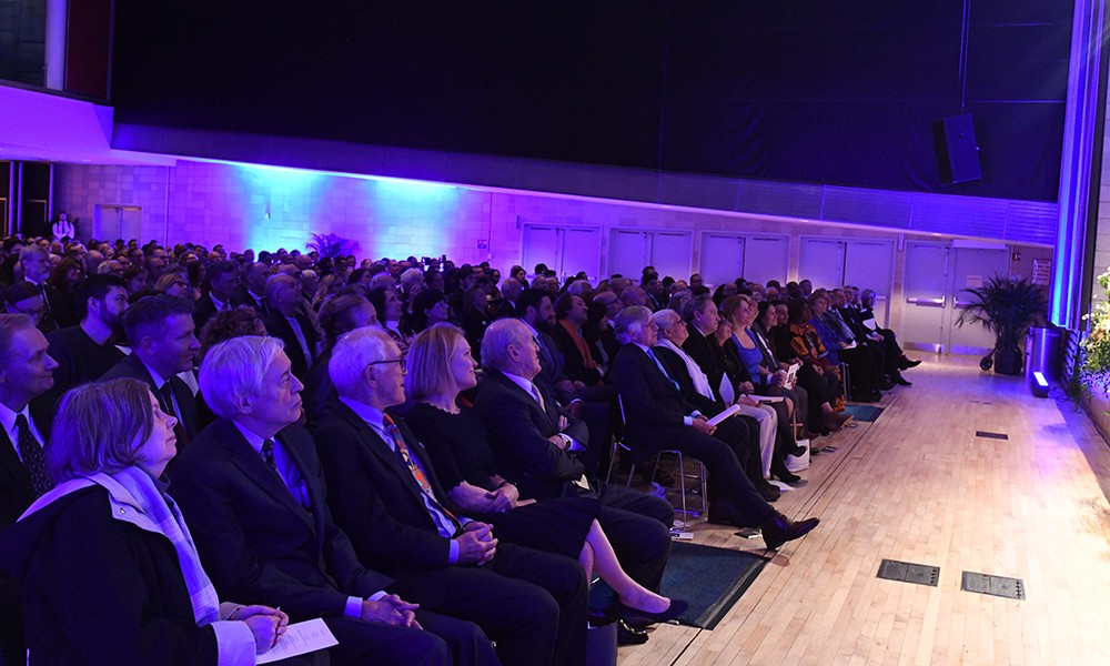 Photo of the audience bathed in purple light, looking up at the stage at Peter Awn's memorial