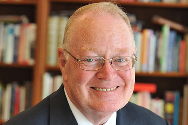 Photo of John Coatsworth, a man with glasses in a suit.