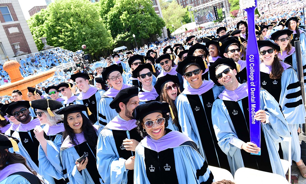 Photo of students in academic regalia with purple hoods, celebrating at Commencement