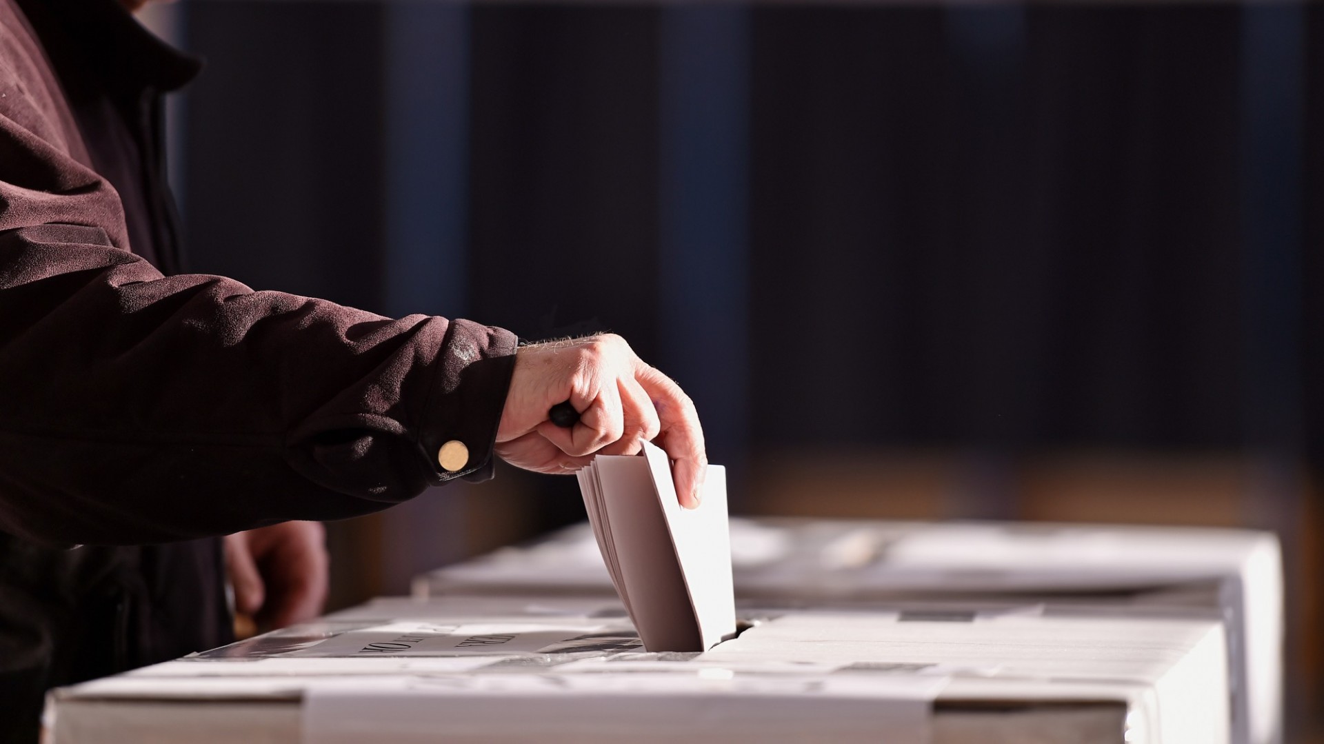 A hand dropping a paper ballot into a ballot box