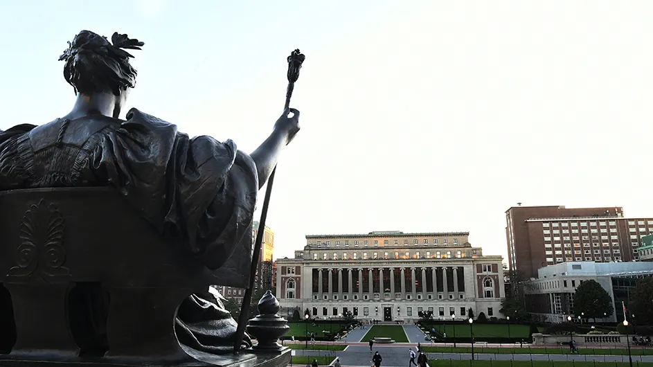 Bronze statue of Alma Mater, a classically-dressed woman sitting with a laurel wreath in her hair and a scepter in her hand, against the backdrop of Butler Library on Columbia's Morningside campus. 
