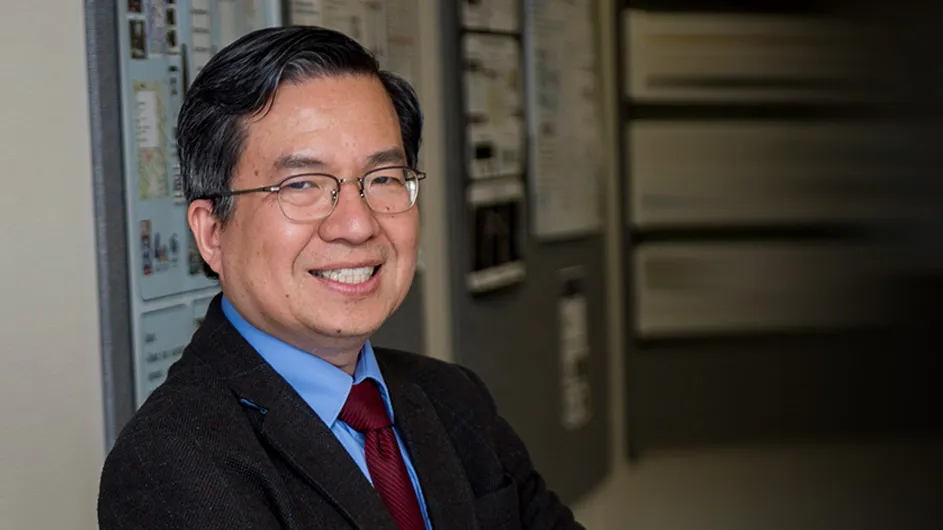 Man with glasses in a dark suit and tie, smiling. 
