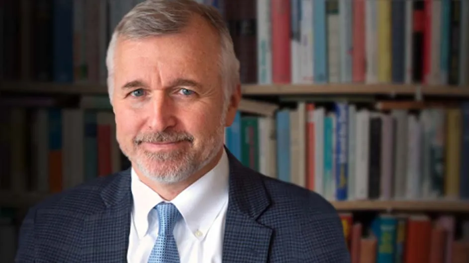 Man with short hair, a mustache and a beard, in a dark suit, light blue tie, and white shirt. 