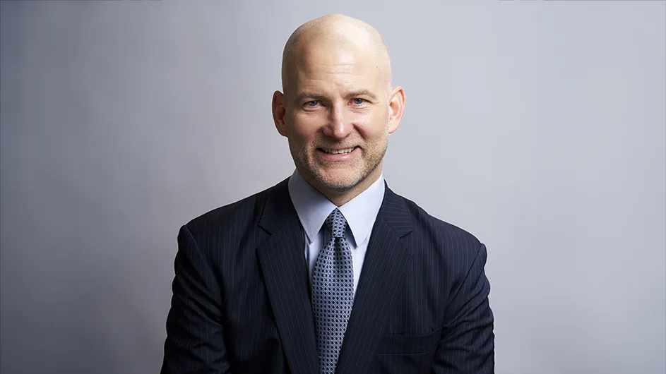 Headshot of a man in a dark suit, smiling. 