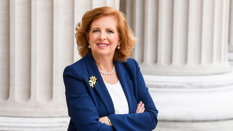 A woman with medium-length red hair in a blue suit, stands outside with arms crossed, against the backdrop of the white marble columns of Low Library on Columbia's Morningside campus. 