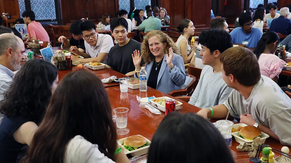 A group of people sitting in a college dining hall, eating and talking. 