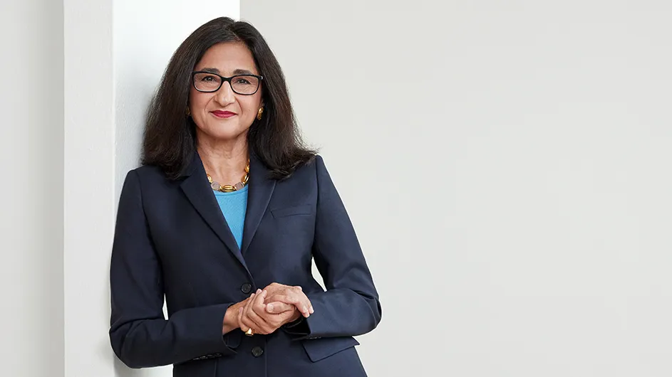 A woman in a blue suit standing against a wall.