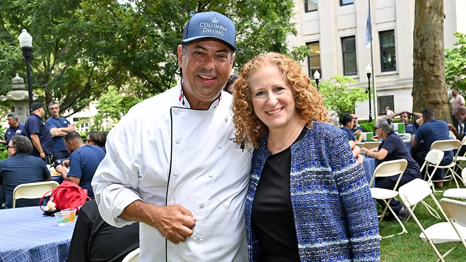 Two people standing outside at a picnic, smiling. 