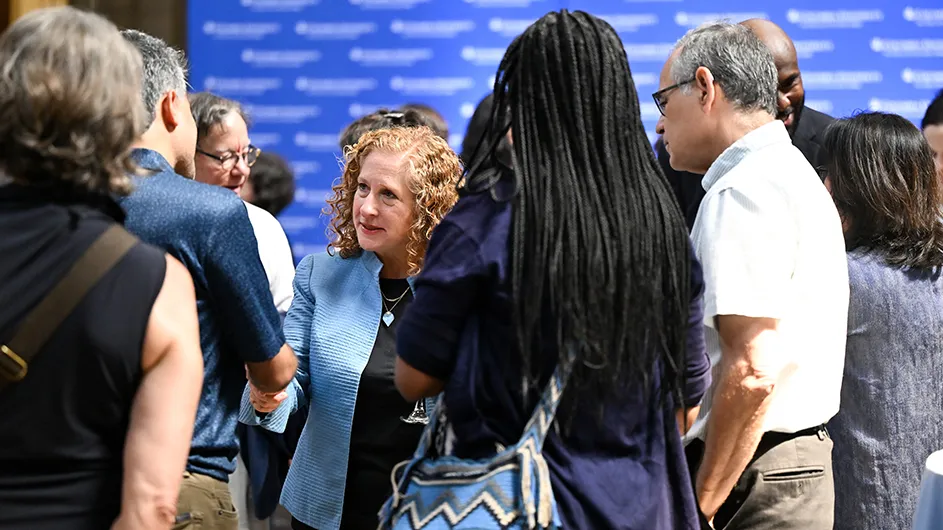 A group of people standing around talking and shaking hands. 