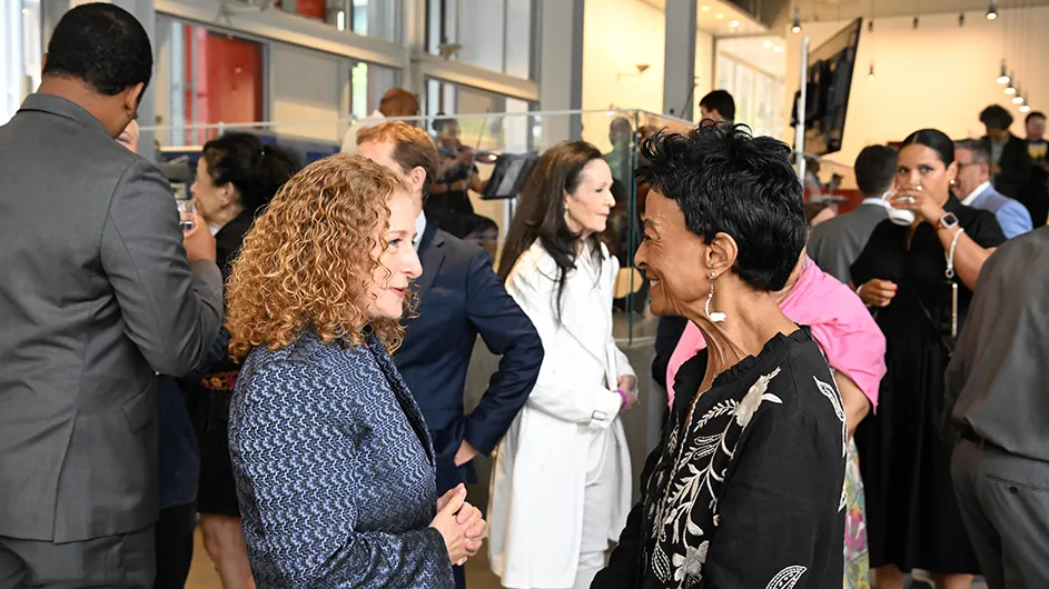 Two women talking in a reception surrounded by people. 