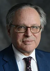 headshot of a man with glasses in a dark suit and tie