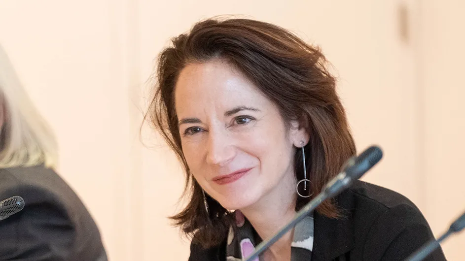 Photo of a woman with mid-length medium brown hair, sitting at a podium